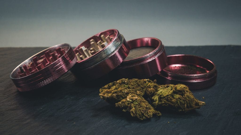 Marijuana buds and joint lie on a dark gray background. Grinder near cannabis. 