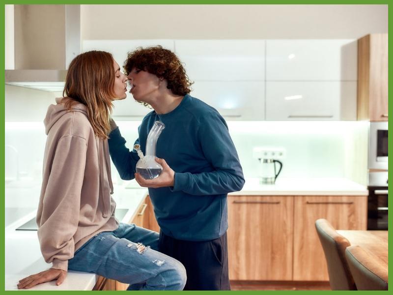 young caucasian couple smoking marijuana together in a modern kitchen about to kiss with smoke coming out of mouth