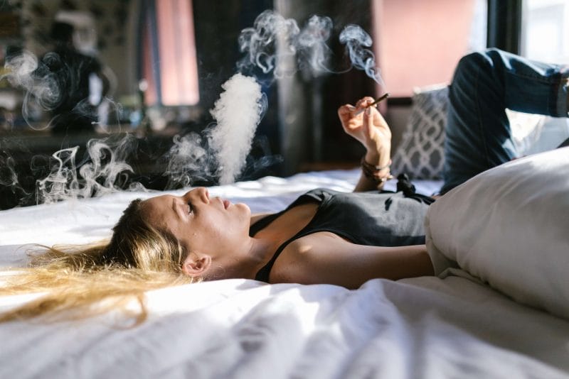 woman laying on back in bed with blonde hair smoking weed joint trying to cure hangover